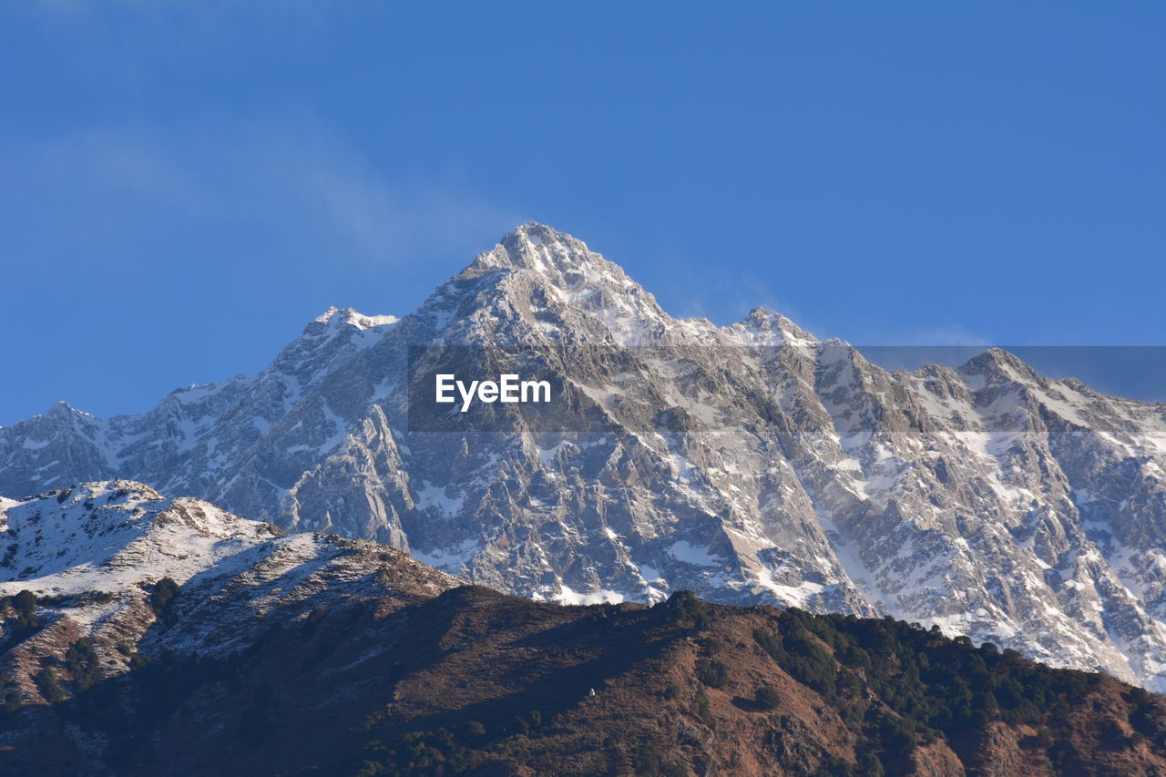 Low angle view of snowcapped mountains against clear blue sky