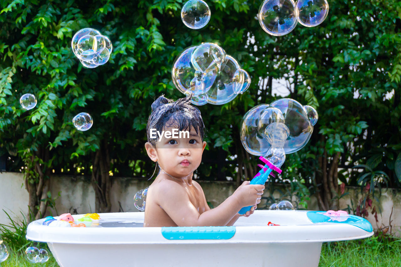 Portrait of smiling boy with bubbles in bathtub at yard