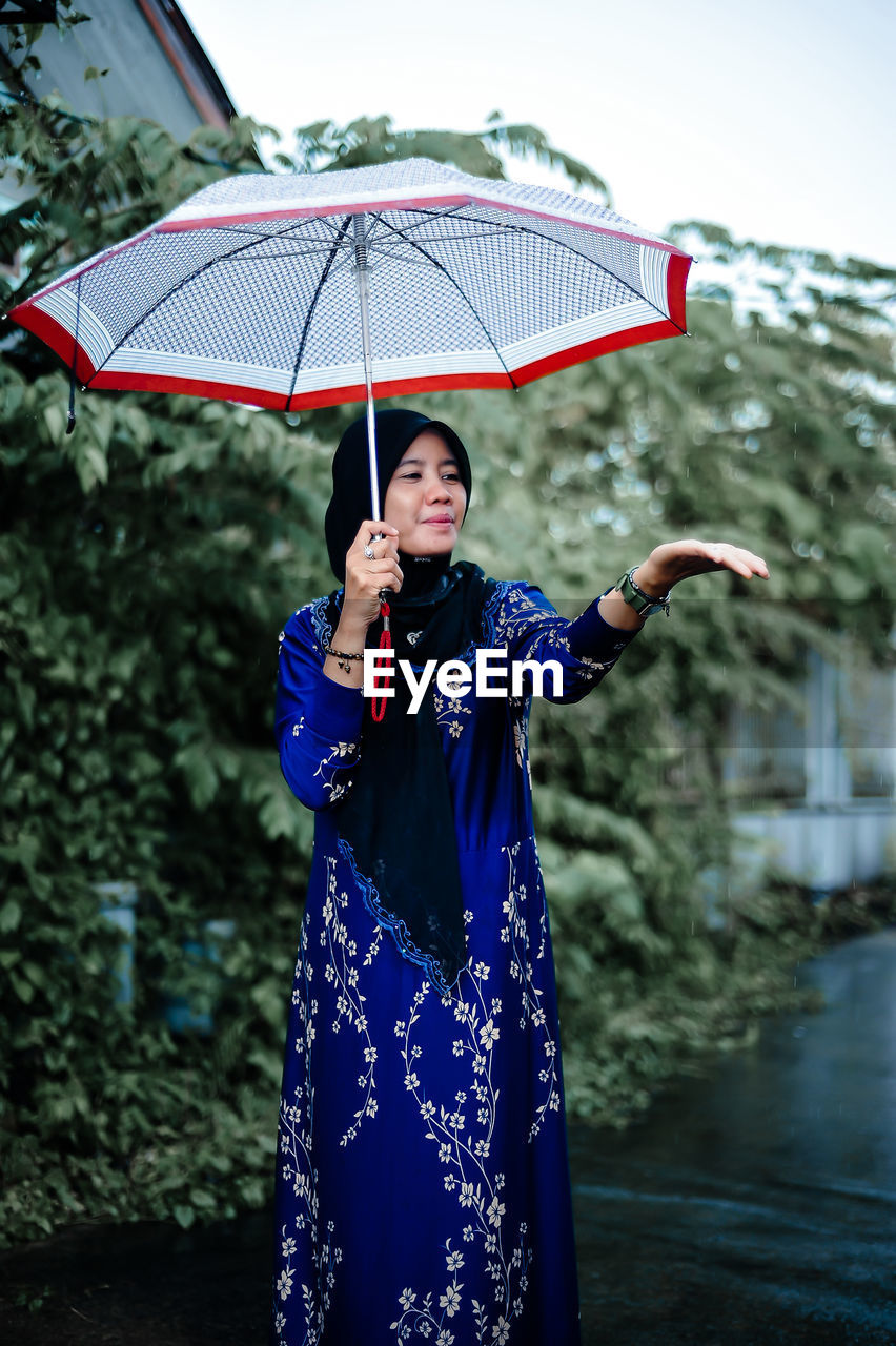 Rear view of woman with umbrella standing against wall