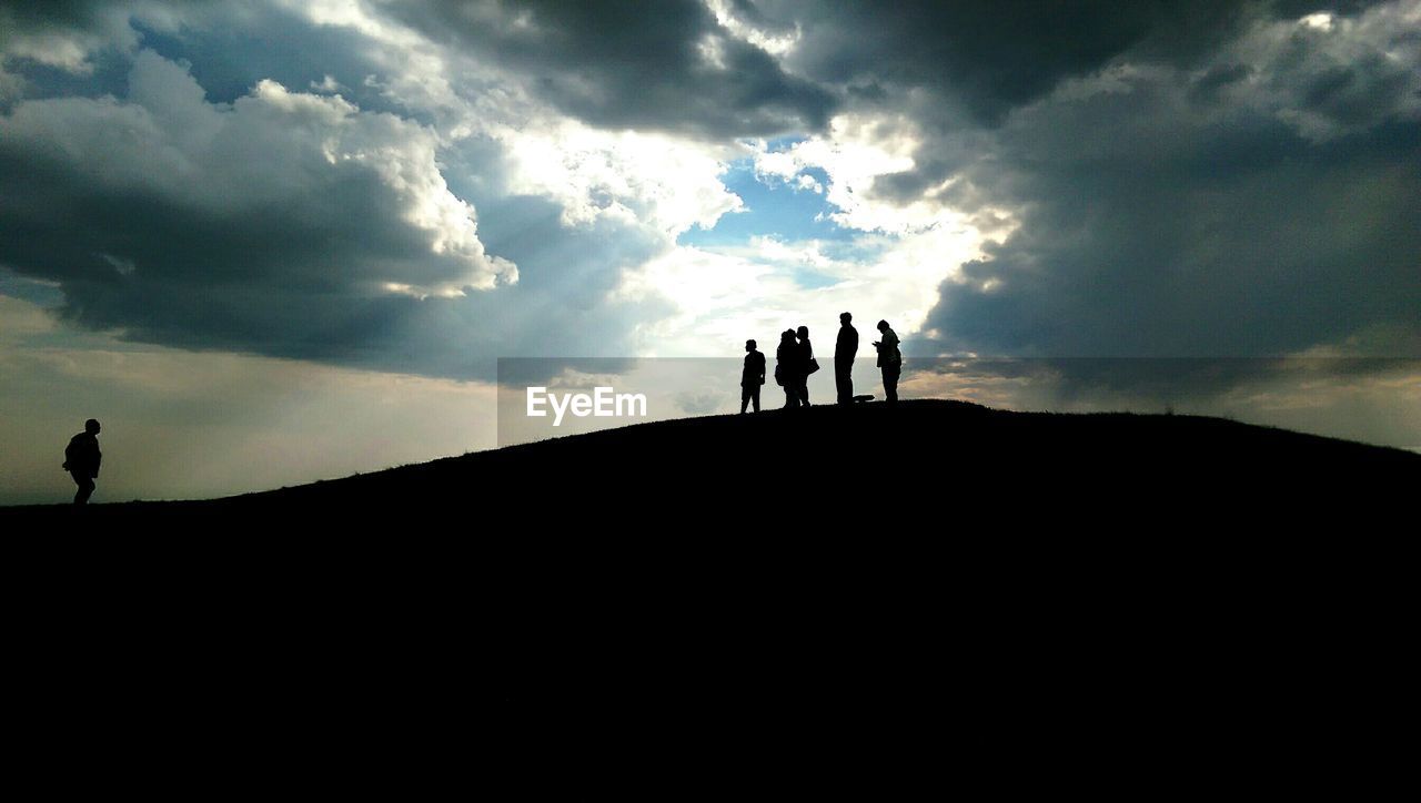 Silhouette people on hill against cloudy sky