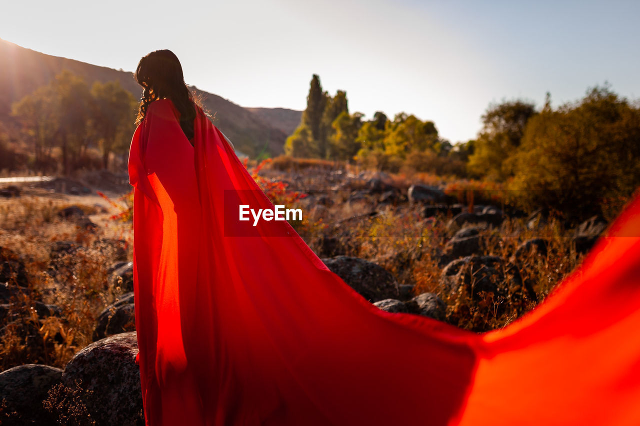 MIDSECTION OF WOMAN STANDING BY RED UMBRELLA AGAINST SKY