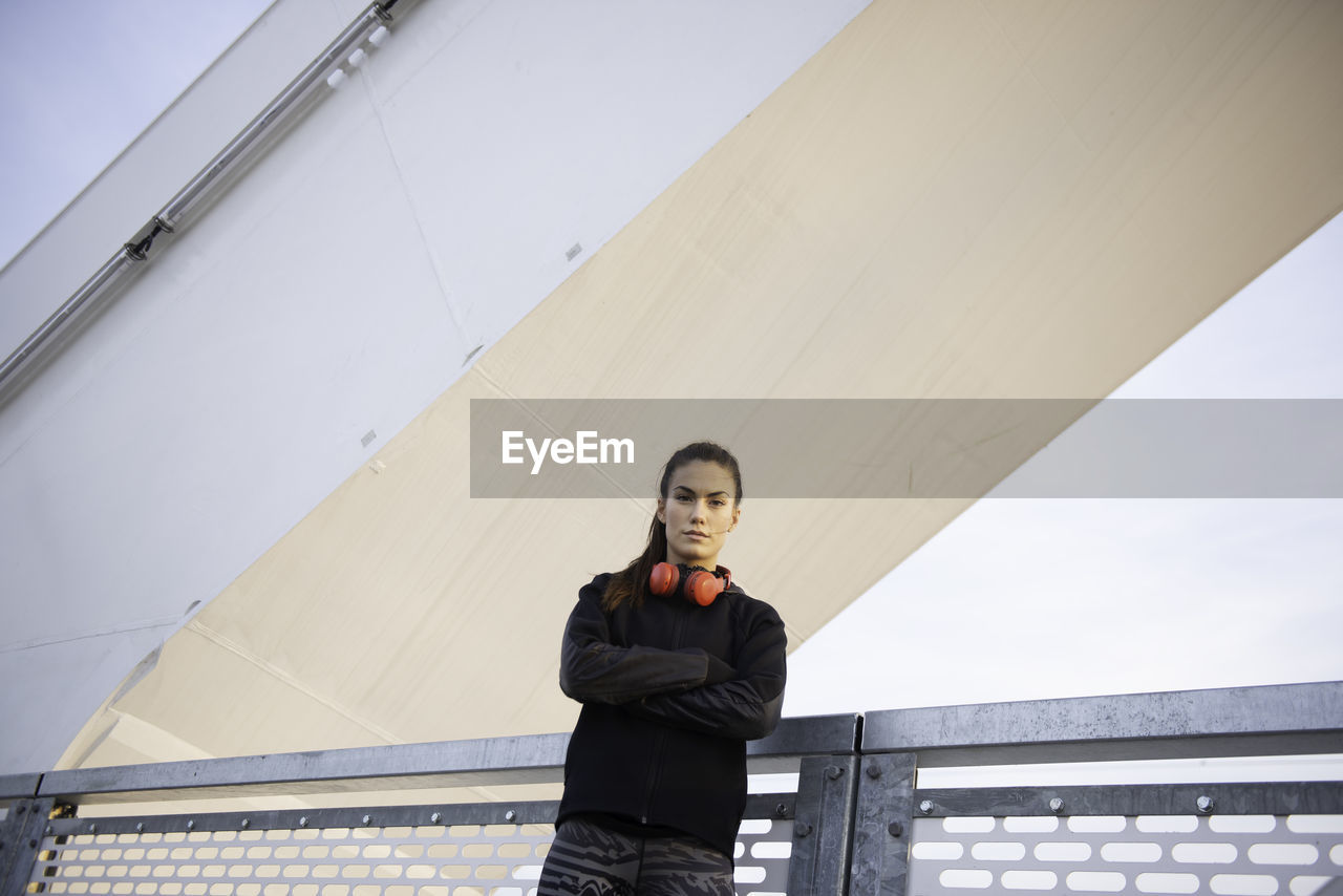 PORTRAIT OF YOUNG WOMAN STANDING AGAINST RAILING