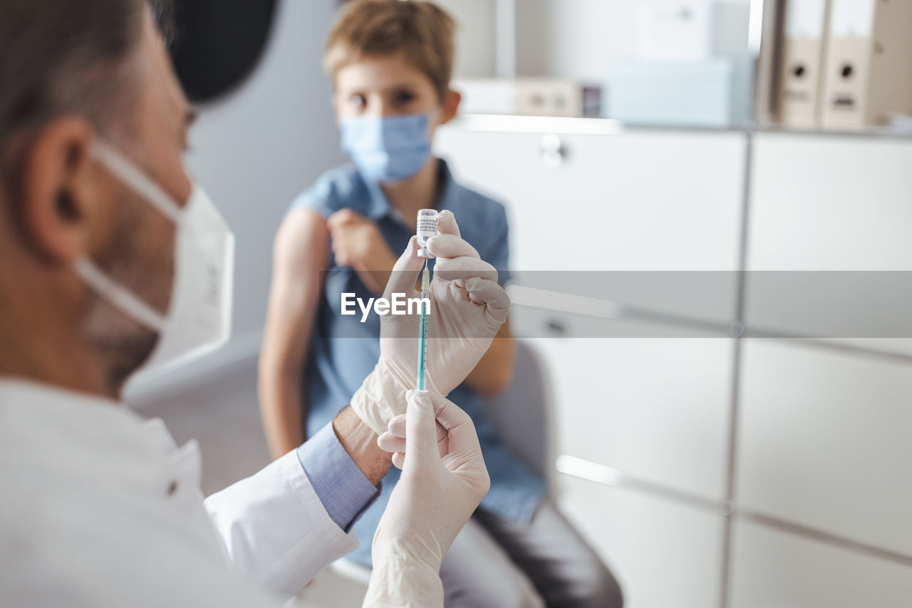 Healthcare worker preparing vaccine syringe for boy in background