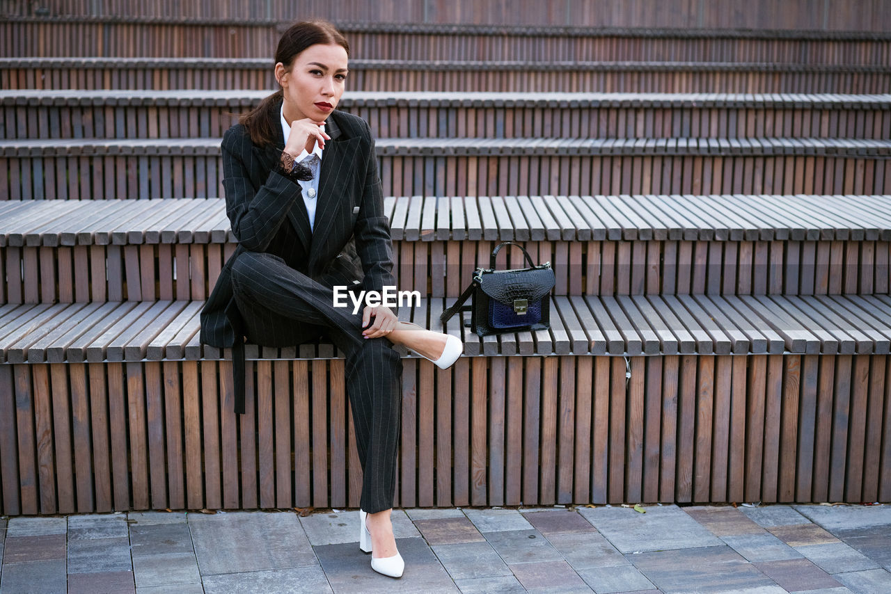 Business woman sitting on a bench in a suit and bag