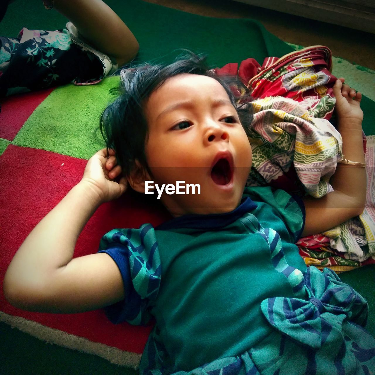 High angle view of cute baby girl yawning while lying on bed at home