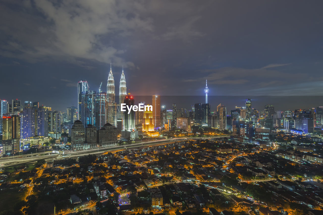 Illuminated buildings in city against cloudy sky