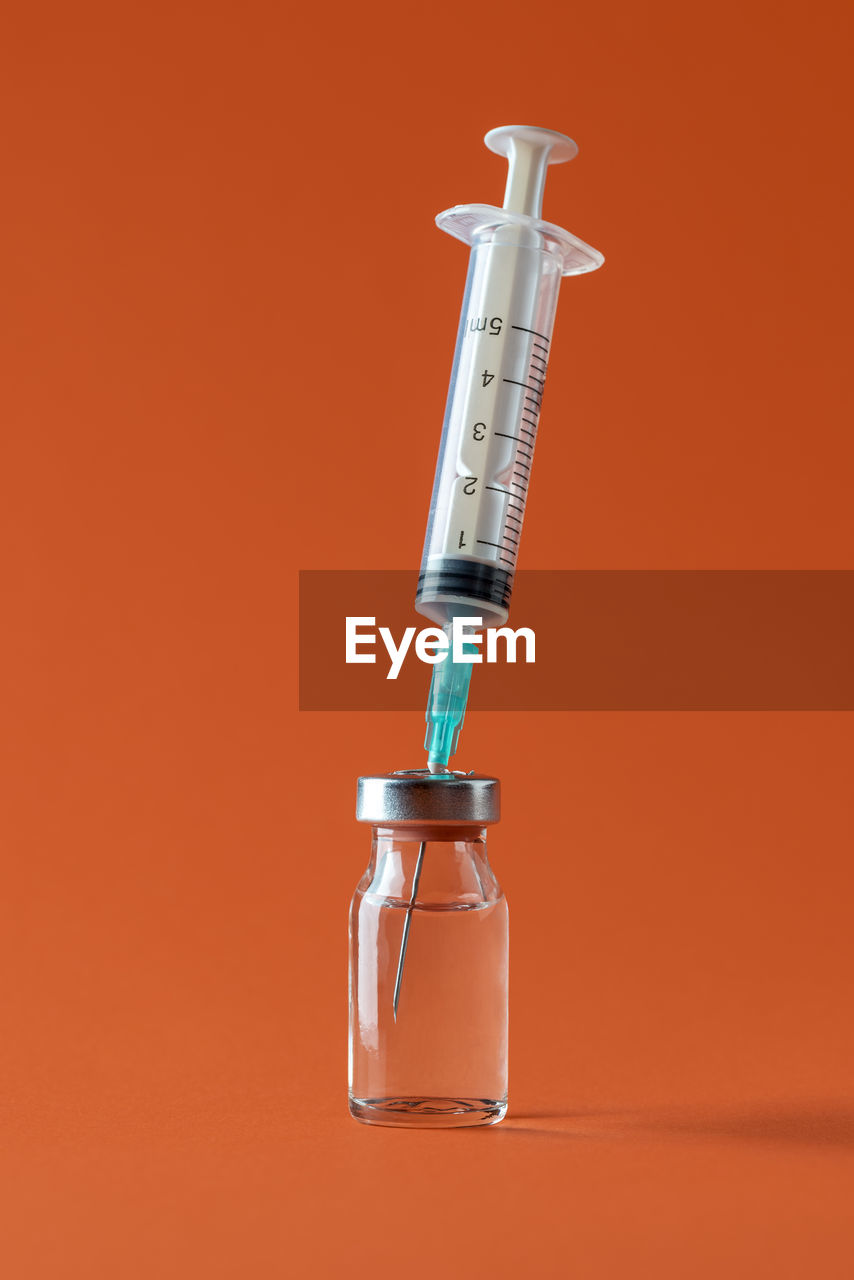 Bottle with medication drug and a syringe with needle minimalist on orange background. vaccine vial