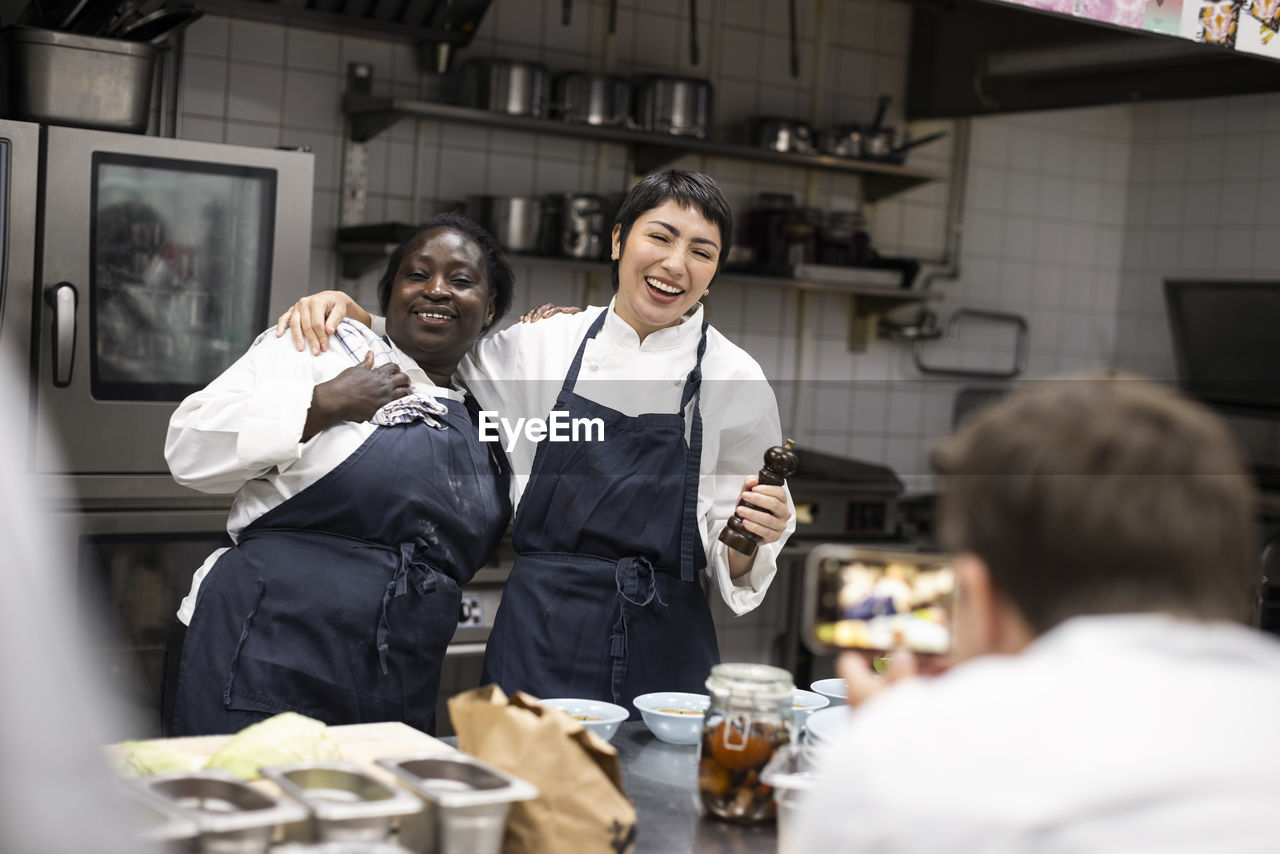 Male chef photographing happy colleagues at commercial kitchen