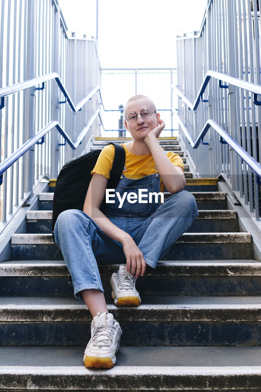 Androgynous person with backpack sitting on staircase