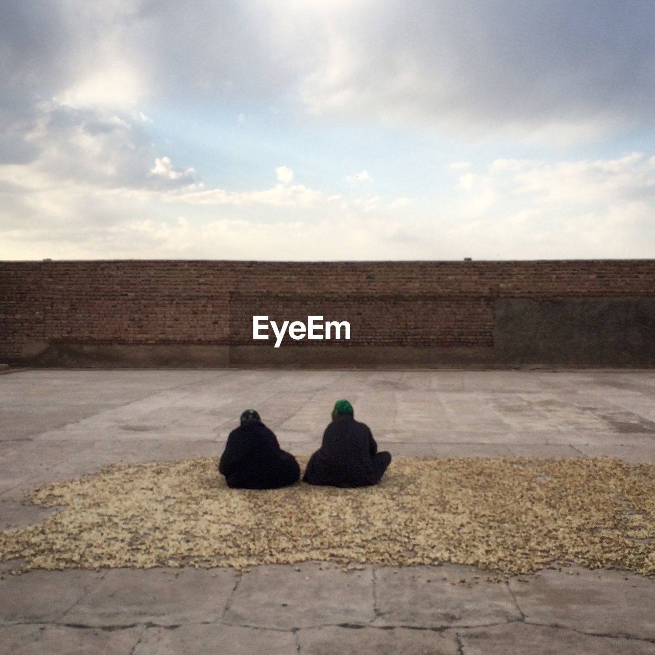 Rear view of women in hijab sitting on building terrace against cloudy sky