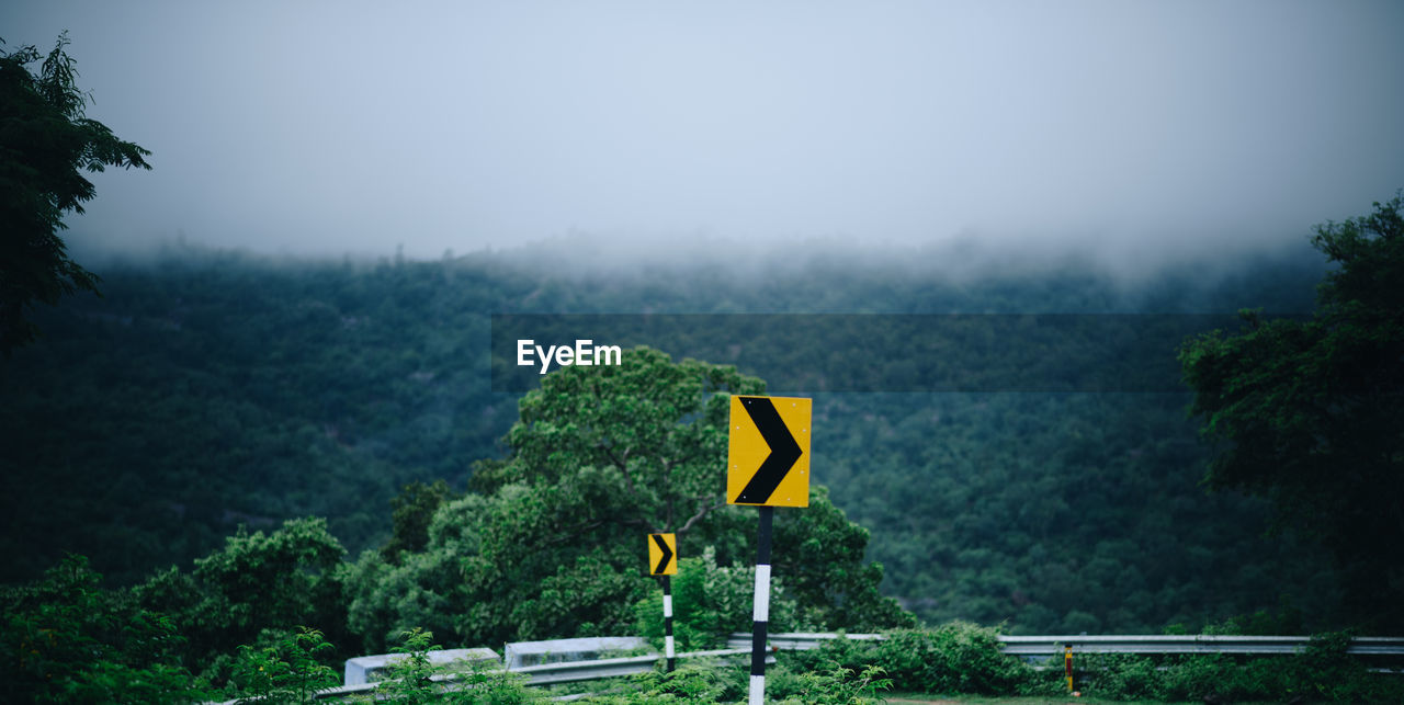 Yellow road sign on mountain against sky