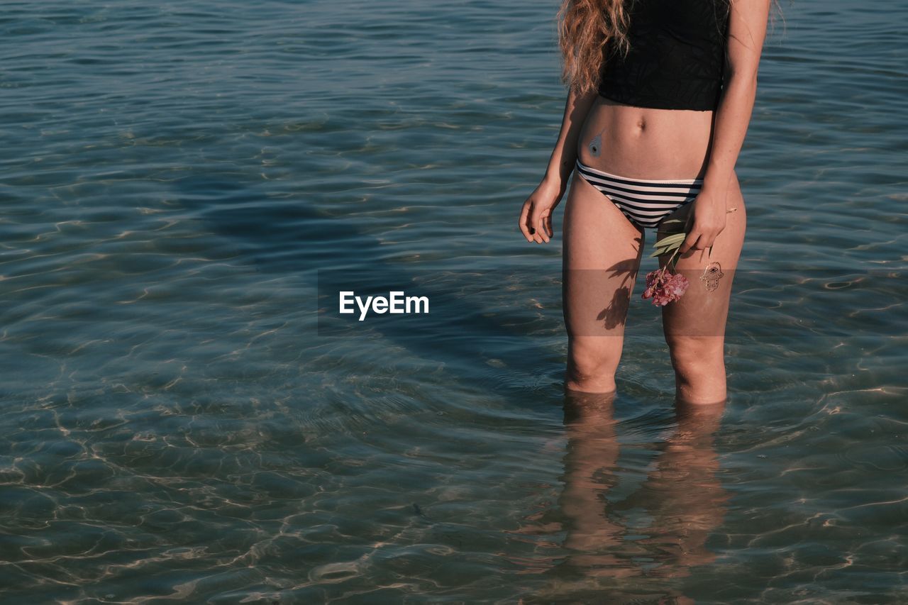 Midsection of woman with flower standing in sea