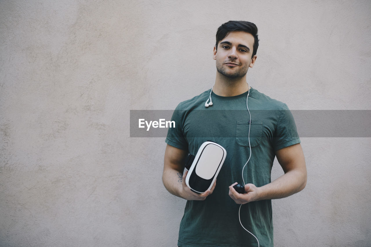 Portrait of computer programmer holding vr glasses and remote control against beige wall in office