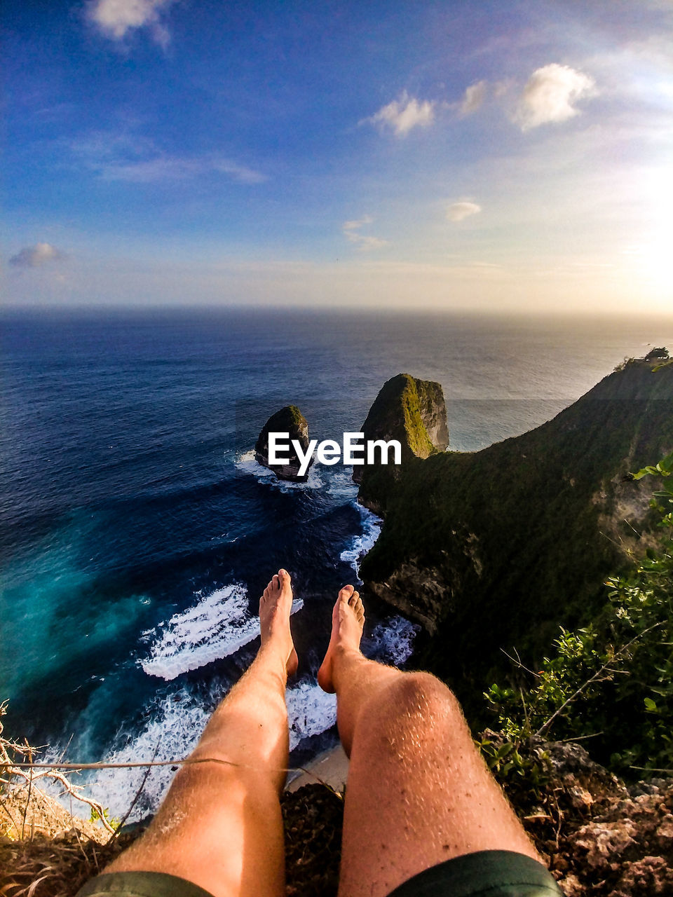 Low section of man relaxing on rock over sea against sky