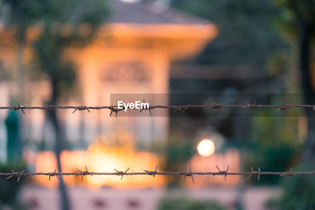 Close-up of barbed wire fence during sunset