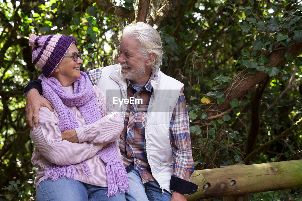 Smiling senior couple sitting by tree outdoors