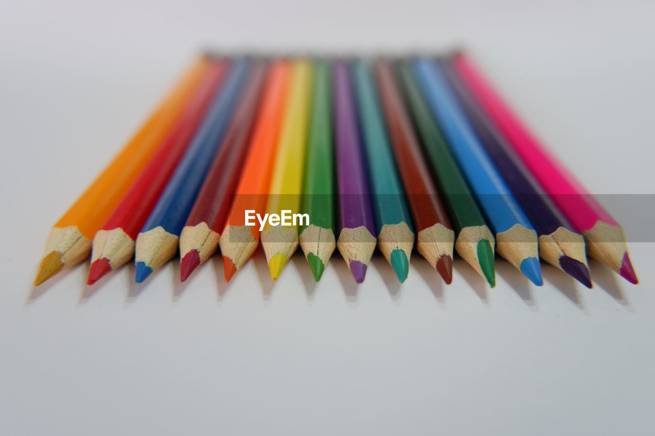 HIGH ANGLE VIEW OF COLORED PENCILS AGAINST WHITE BACKGROUND