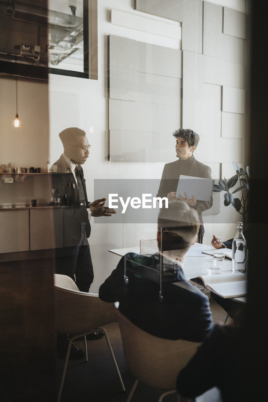 Businessman planning strategy with colleagues in board room seen through glass