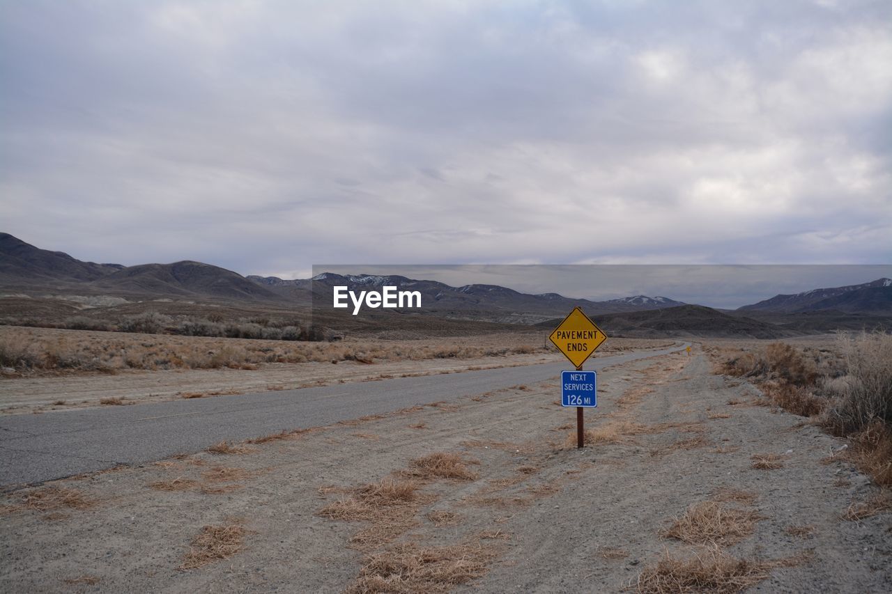 Road sign on road against sky