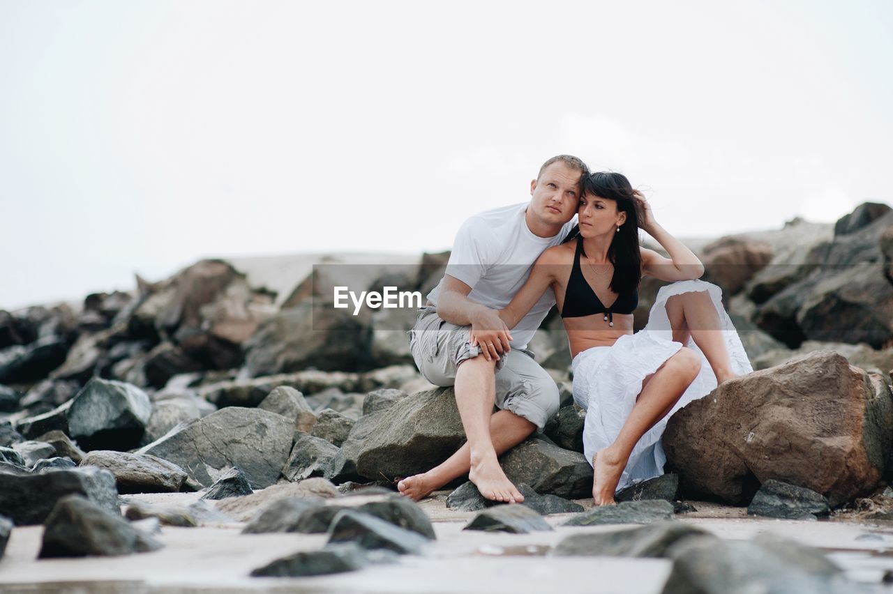 Couple sitting at beach against sky