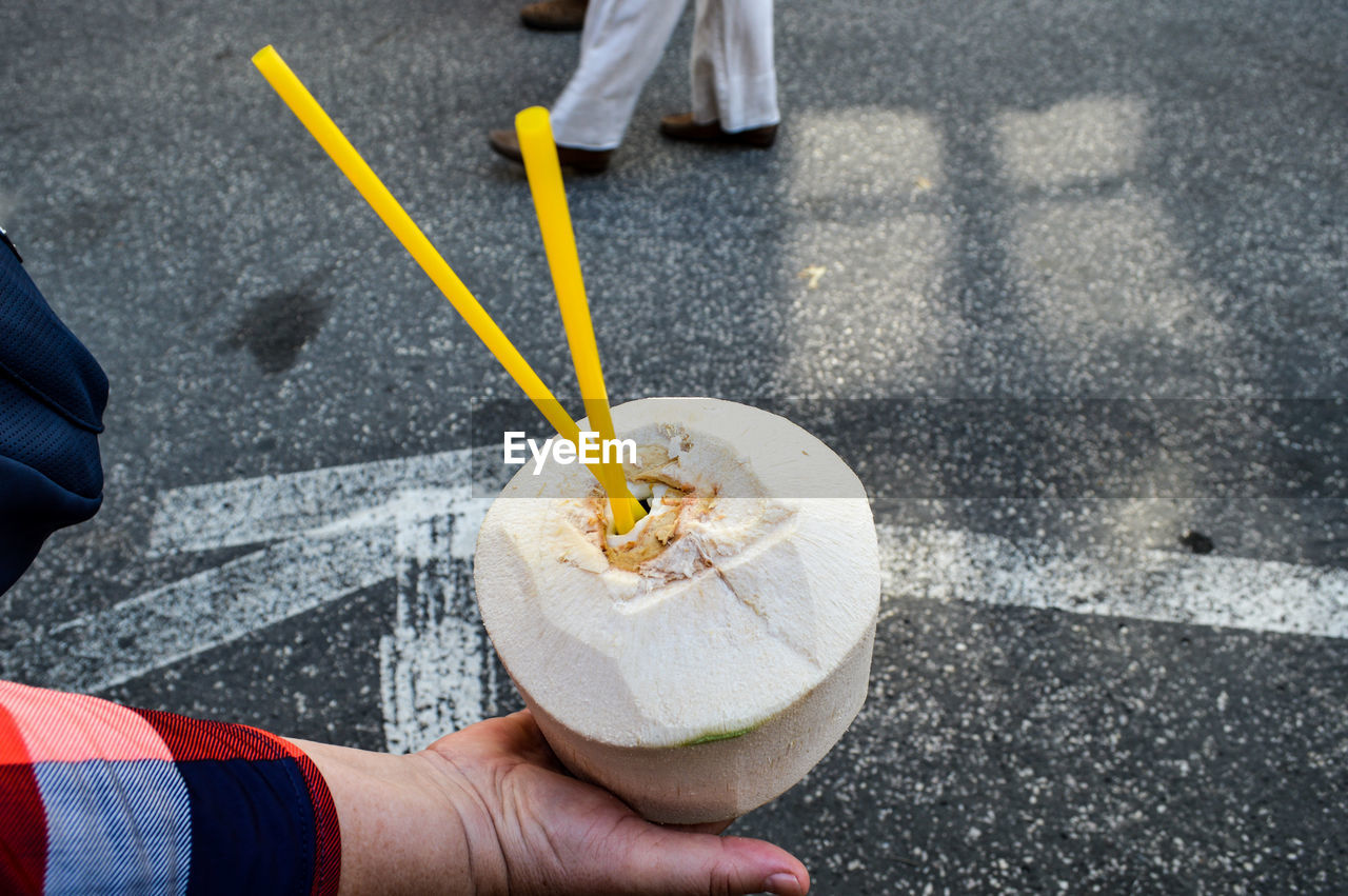 Cropped image of hand holding coconut on street