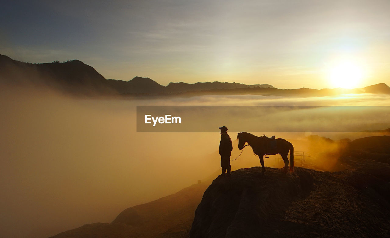 Silhouette man and horse on mountain cliff