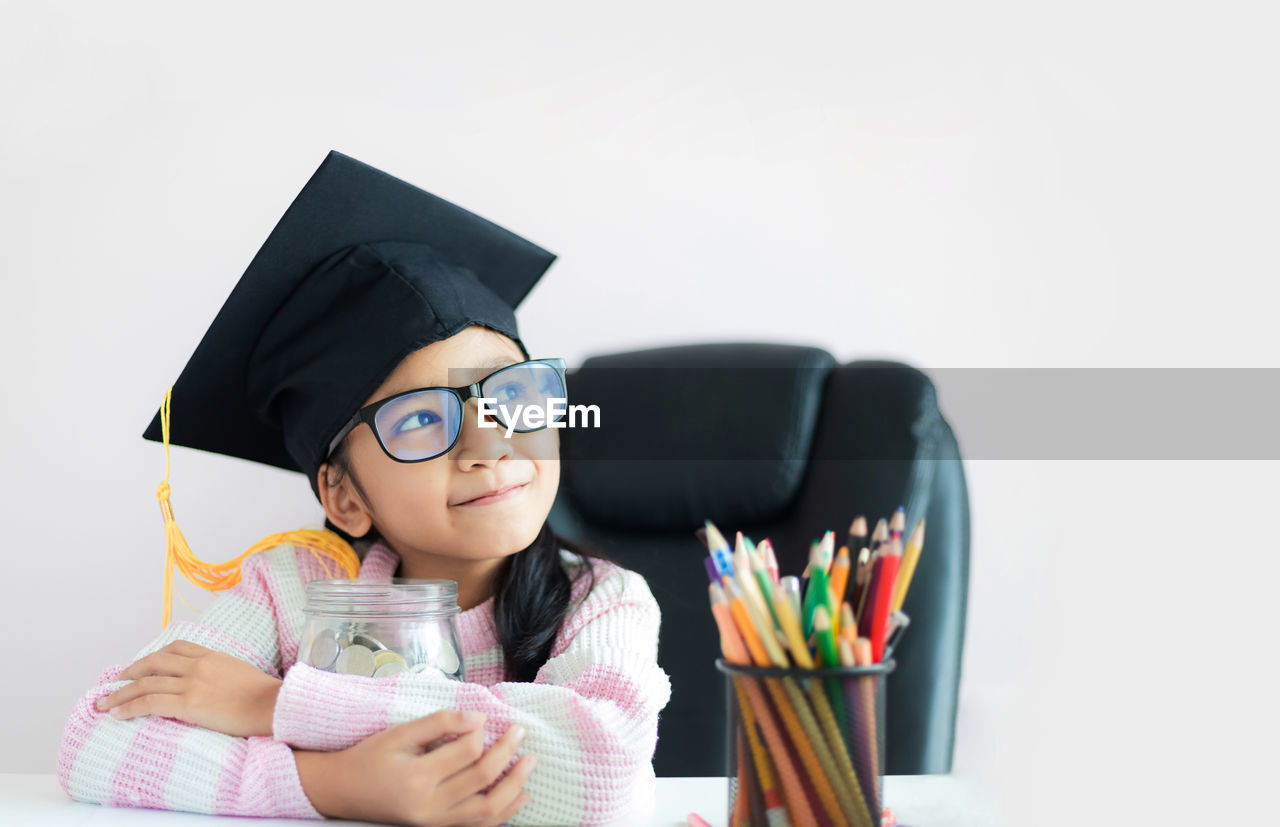 Smiling girl looking away while holding coins in jar on table