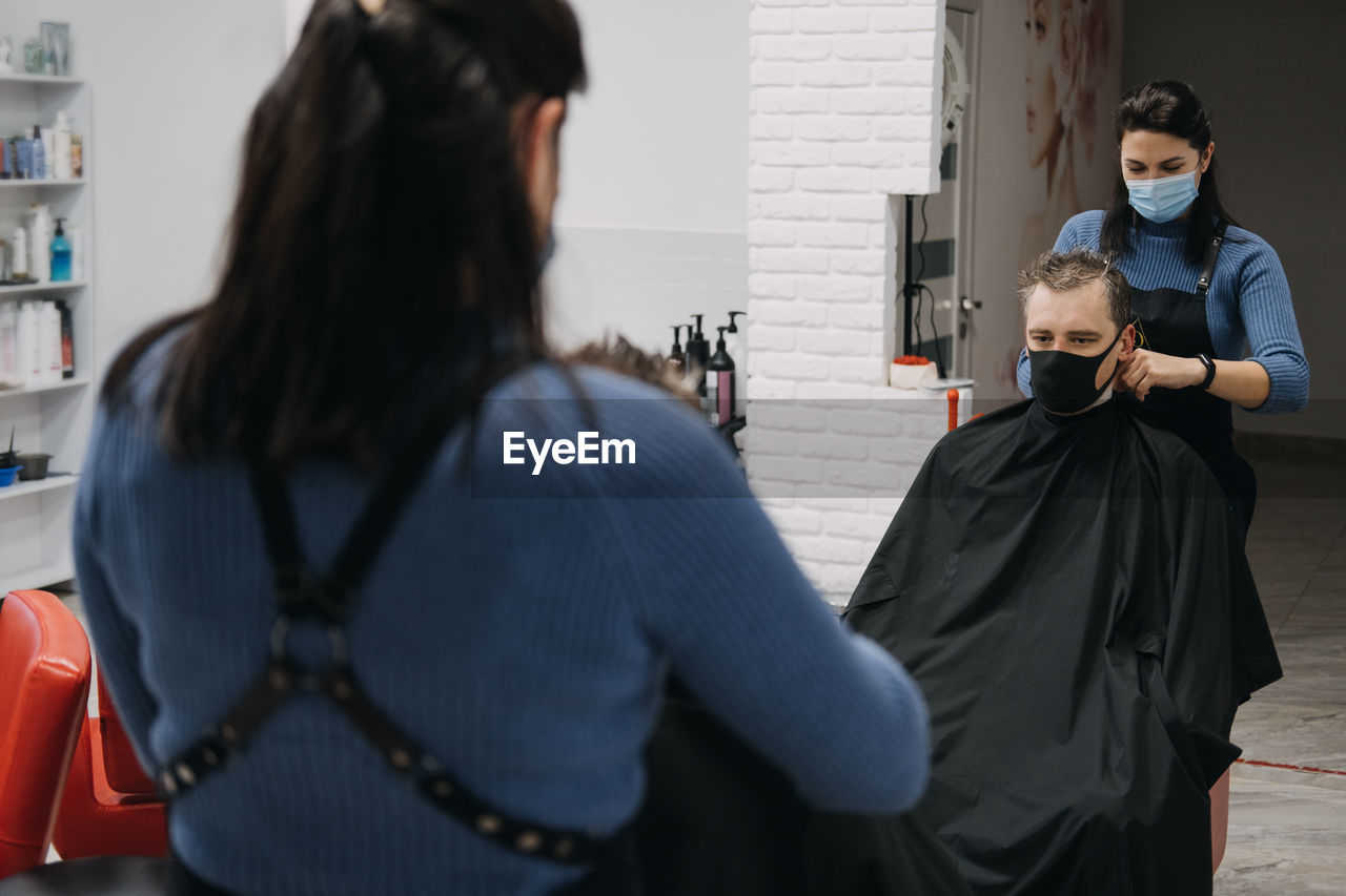 Female barber wearing mask cutting hair of customer