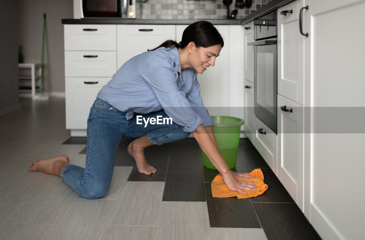 Cheerful woman washing floor in kitchen