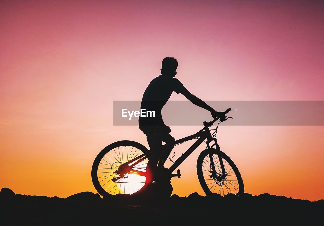 Silhouette man on bicycle against sky