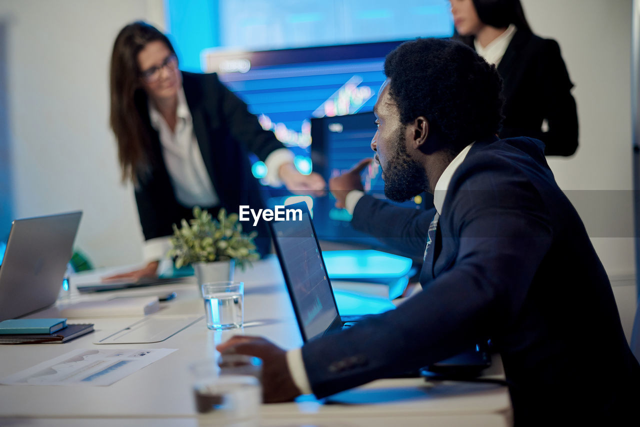 Crop multiracial employees working at table with laptops in office