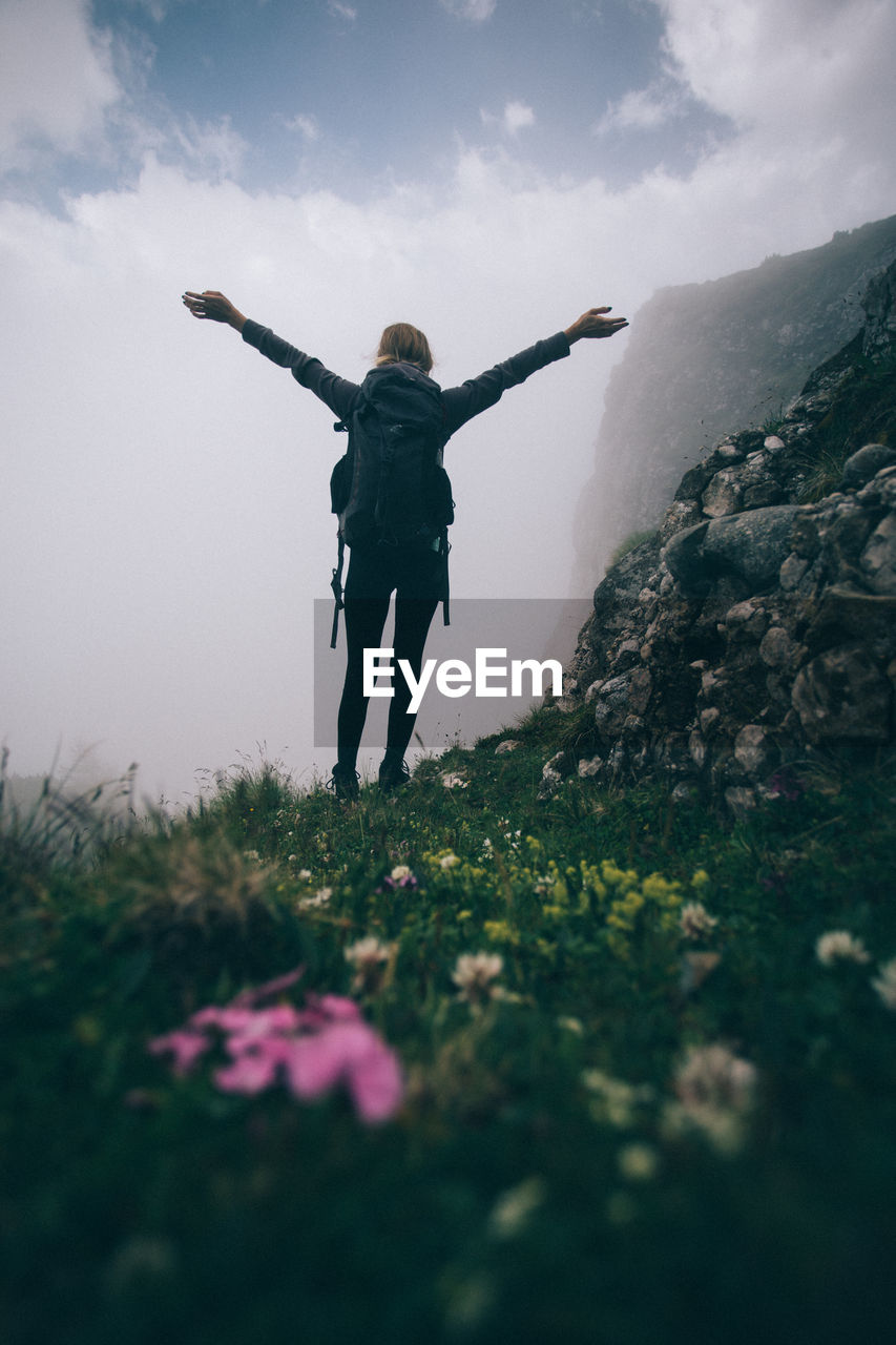 Rear view of woman with arms raised standing on landscape against sky