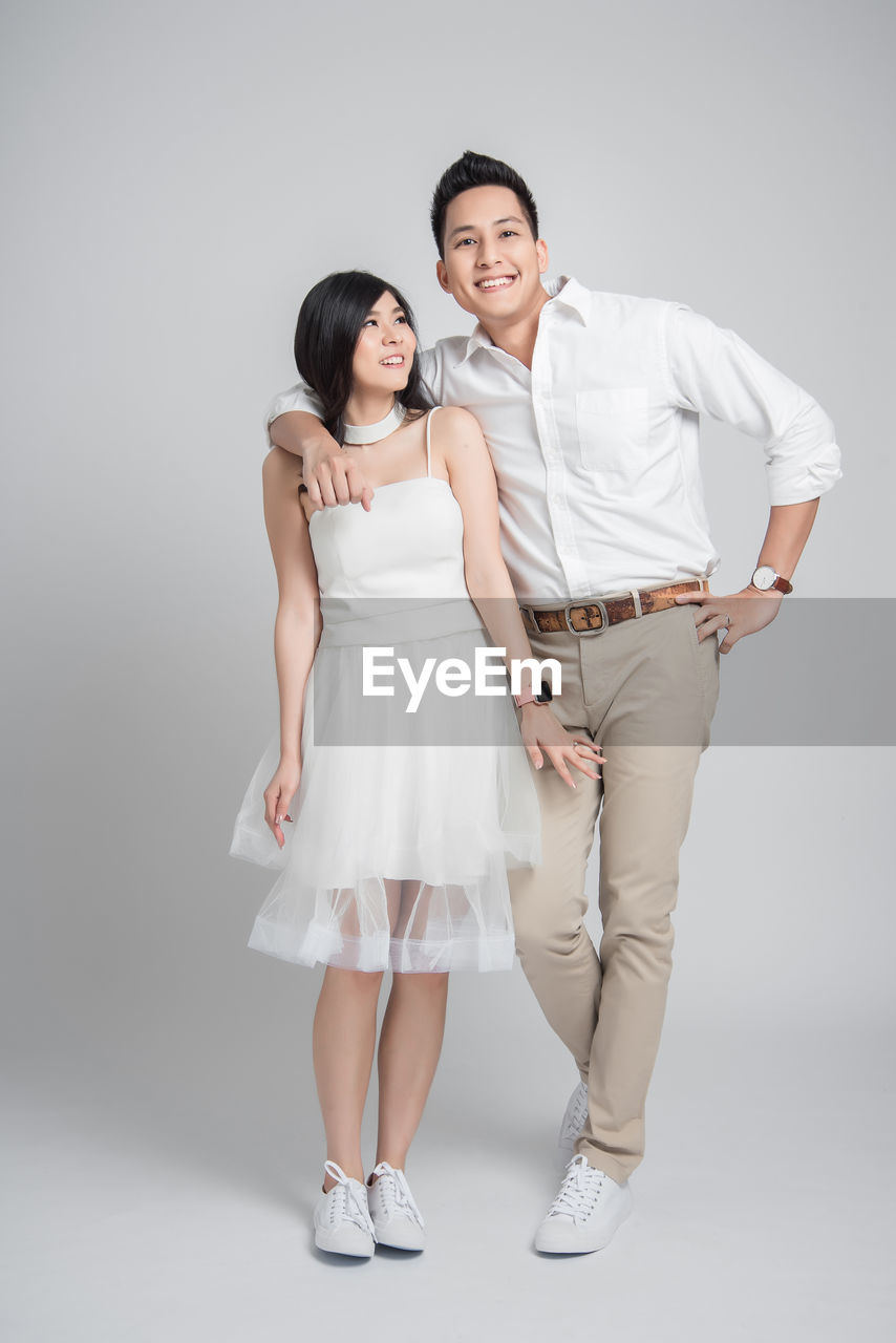 Full length portrait of smiling couple standing over gray background
