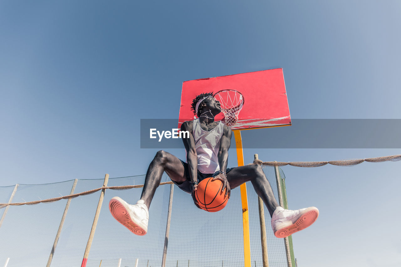 Low angle view of basketball player jumping against clear sky