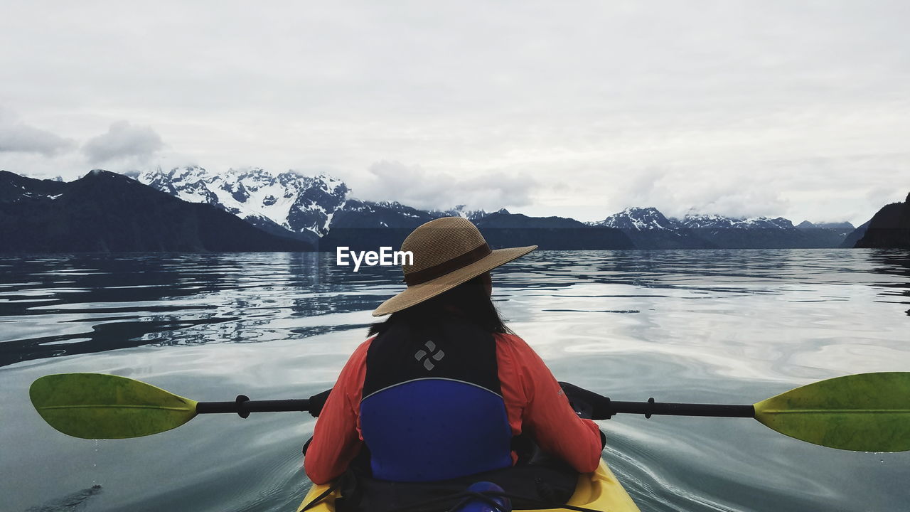Rear view of woman kayaking in river against mountains during winter