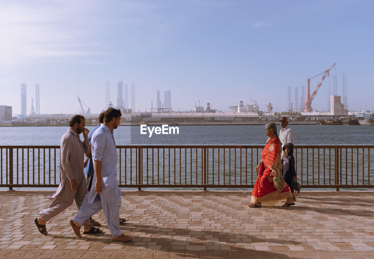 REAR VIEW OF PEOPLE AT SEA AGAINST SKY