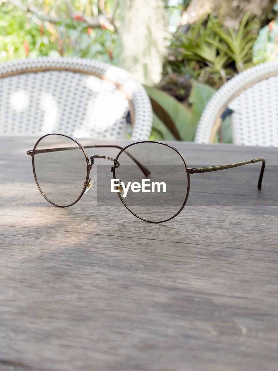 CLOSE-UP OF EYEGLASSES ON TABLE AGAINST PLANTS