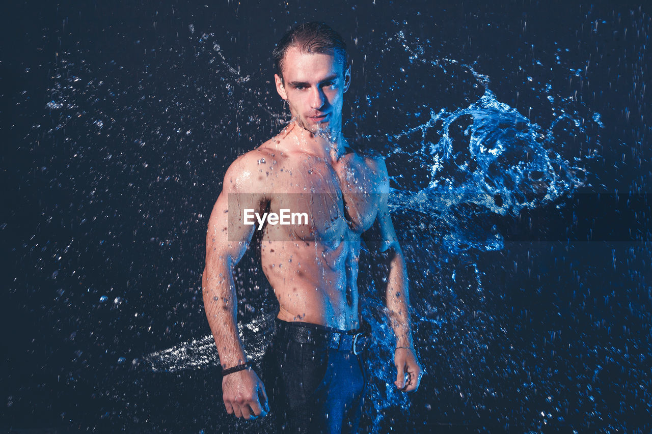 Portrait of shirtless man standing against black background