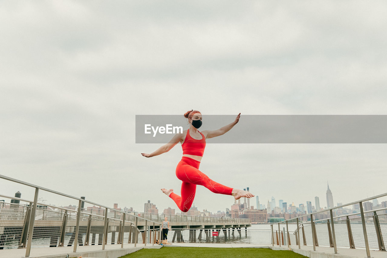 Young female athlete jumping mid air wearing face mask by waterfront