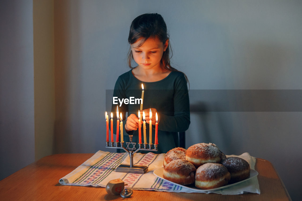 Girl lighting candles on menorah for traditional winter jewish hanukkah holiday at home. 