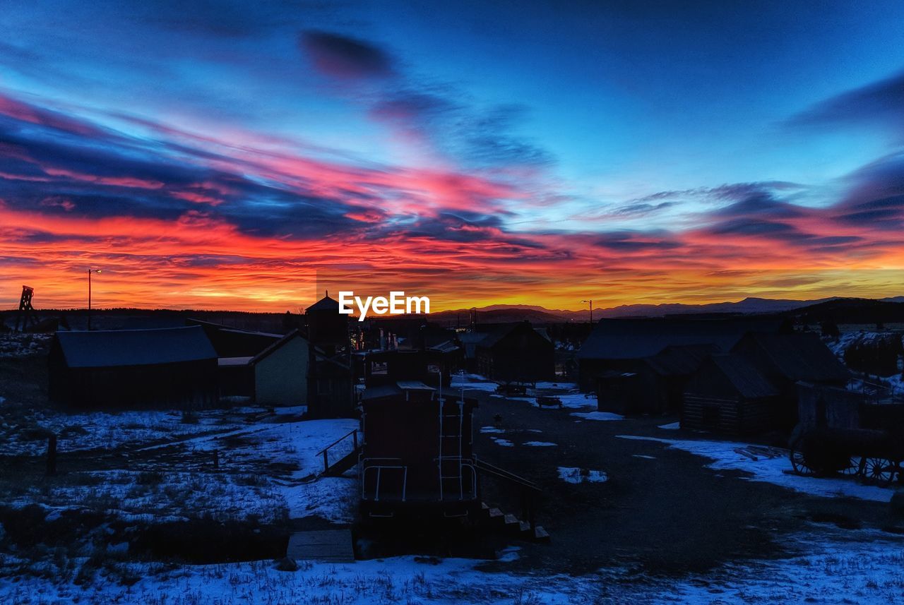 HOUSES ON FIELD DURING WINTER AGAINST SKY