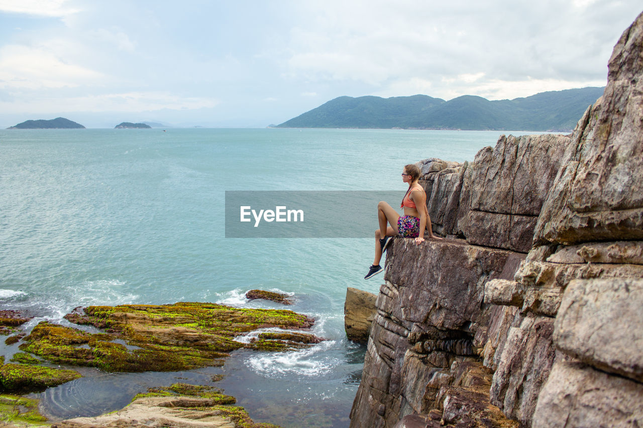 Scenic view of sea and mountains against sky with woman sitting on rocks