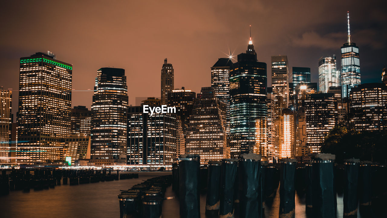 Illuminated buildings by river against sky at night