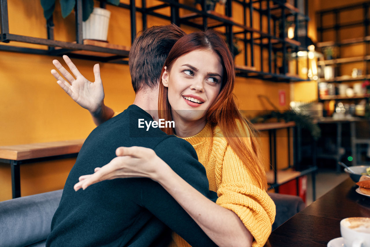 Portrait of smiling woman looking away while embracing at cafe
