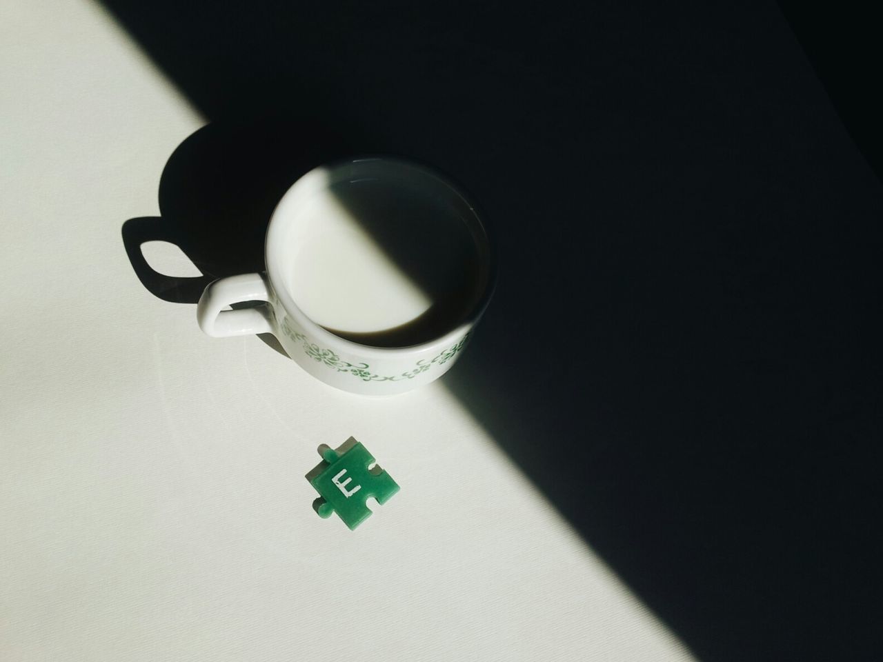 High angle view of milk cup and jigsaw piece on white table