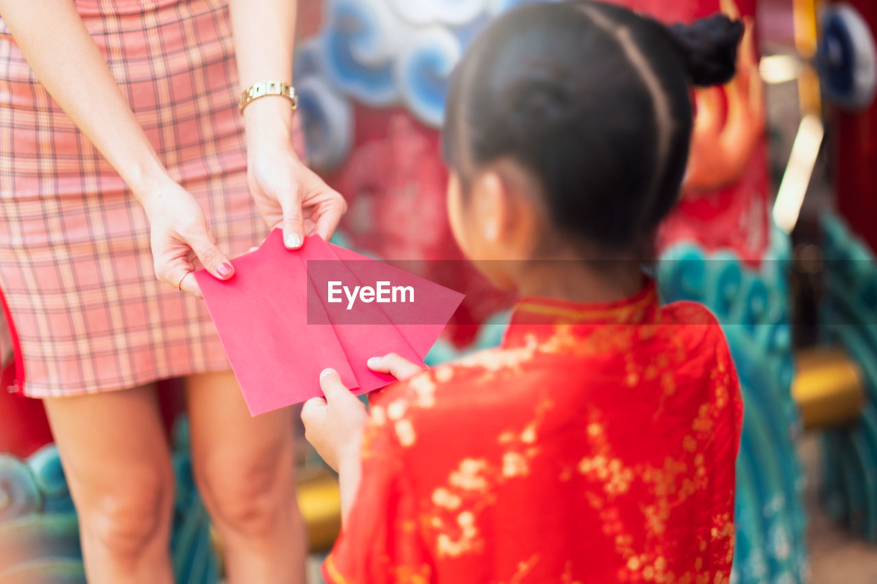 Midsection of woman giving red envelope to girl during chinese new year