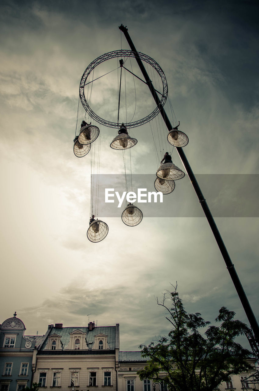 Low angle view of lanterns hanging against cloudy sky in city