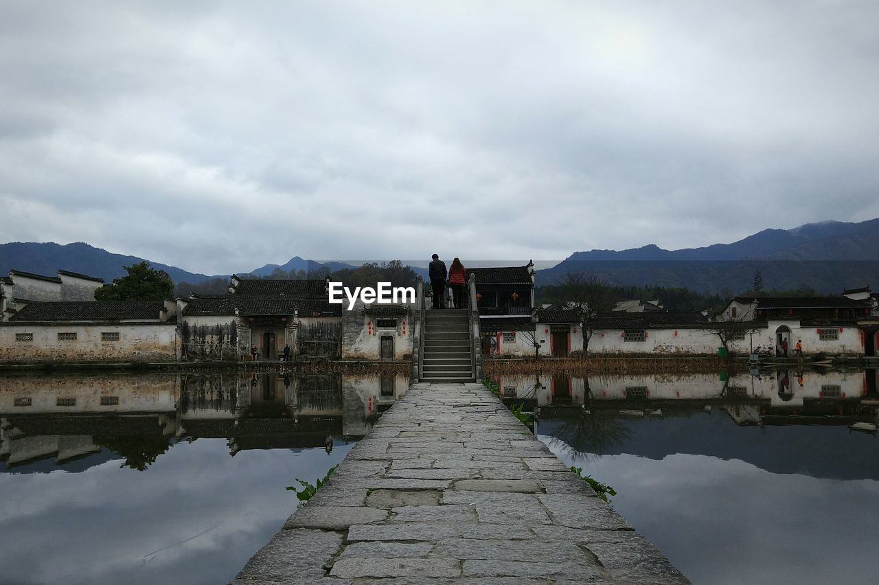 Walkway amidst lake against cloudy sky at dusk