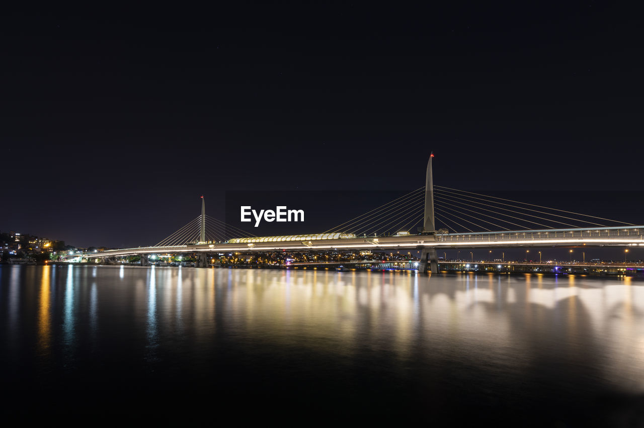 Illuminated bridge over river against sky at night