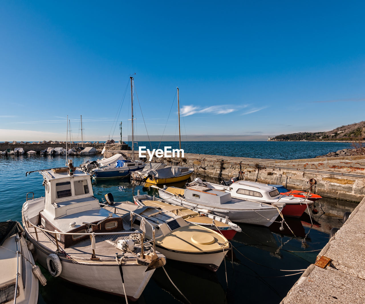 Sailboats moored at harbor against blue sky